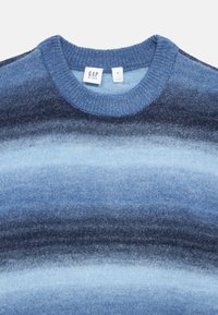 Kötött pulóver kék árnyalatokban, fokozatos színátmenettel; kerek nyakkivágás bordázott mintával. A textil puha tapintásúnak tűnik, enyhe fémes csillogással. Látható márkajelzés.