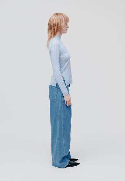 Maglietta a maniche lunghe a coste blu chiaro e jeans in denim a gamba larga con vita alta. Scarpe nere a punta completano il look. Texture liscia.