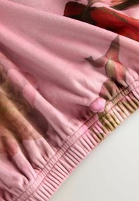 Ružová kvetinová tkanina s jemnou, zamatovou textúrou. Má na konci zošitý elastický lem a vzory ruží v akvarelovom štýle v rôznych odtieňoch.