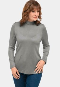 Grauer langärmeliger Pullover mit hohem Kragen, ausgestattet mit Seitentaschen und dezenten Steppnähten entlang der Taschen für zusätzliche Details.