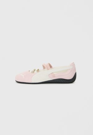 Chaussure slip-on rose en suede avec des accents blancs, semelle en caoutchouc et sangles élastiques. Présente un design texturé et un petit logo sur le devant.