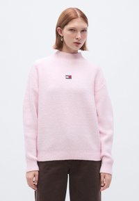 Pulover roz tricotat cu guler înalt, având un mic logo brodat. Modelul este cu nervuri și are un finisaj moale, texturat.