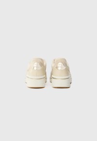 Beige sneakers with a smooth leather upper, metallic accents at the heel, and a thick white sole. Textured details on the sides.