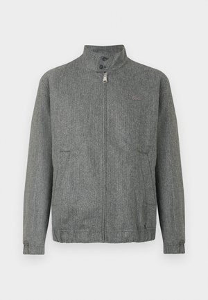 Grau gestreifte Jacke mit Stehkragen, Frontreißverschluss und zwei Seitentaschen. Mit subtiler Logo-Applikation auf der Brust. Strukturiertes Stofffinish.