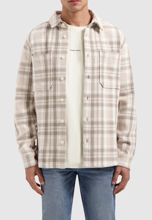 Beige en bruine geruite shirt met een knoopsluiting aan de voorkant, twee borstzakken en een zachte textuur, gedragen over een lichte t-shirt.