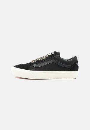 Black canvas sneakers featuring a white rubber sole, metallic decorative laces, and a side logo. Low-top design with smooth texture.
