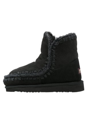 Botină de gleznă din suede negru, cu vârful rotunjit, căptușeală din blană și cusături decorative pe marginea superioară. Talpă plată din cauciuc pentru stabilitate.