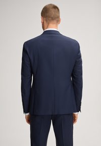 Giacca da completo blu navy con taglio su misura, rever a lancia e uno spacco posteriore singolo. Tessuto liscio con cuciture visibili e bottoni decorativi sulle maniche.