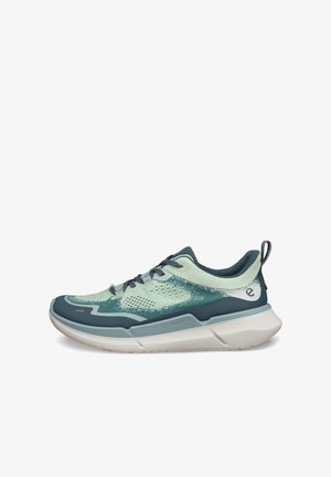 Scarpa da ginnastica atletica verde chiaro e verde scuro con suola bianca imbottita, design con lacci e linguetta posteriore, vista laterale su sfondo bianco.