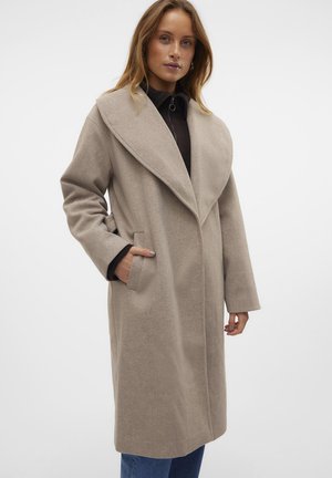 Beige wool blend coat with a wide collar, long sleeves, side pockets, and a loose fit, worn over a dark top and blue jeans.