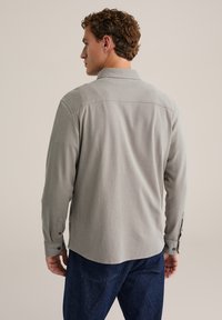 Lichtgrijs shirt met lange mouwen, een kraag, gestructureerde stof, achterpaneel met inzetten en manchetten met knopen, gecombineerd met donkerblauwe spijkerbroek.