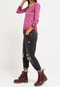 Fuksia pitkähihainen v-pääntie-paita, yhdistetty mustiin kuluneisiin farkkuihin ja viininpunaisiin nauhallisiin saappaisiin, joissa on beige yksityiskohta.