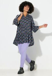 Czarna tunika w kwiatowy wzór, z dekoltem w serek i rękawami do łokcia, zestawiona z liliowymi obcisłymi jeansami i masywnymi czarnymi botkami.