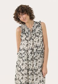 Top floral fără mâneci, de culoare crem cu imprimeu floral negru, cu un decolteu și tiv volanate, dintr-un material ușor, și detaliu în formă de cheie în față.