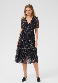 Rochie neagră cu flori, cu mâneci scurte transparente, decolteu tip înfășurare și fustă în straturi. Prezintă un material ușor, fluid, cu un model delicat.
