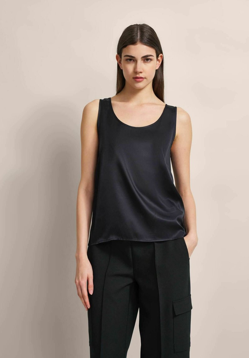 Schwarzes Satin-Top ohne Ärmel mit Rundhalsausschnitt, glatter Textur und lockerer Passform, kombiniert mit schwarzen maßgeschneiderten Hosen mit seitlichen Taschen.