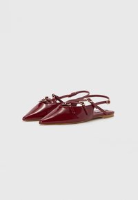 Escarpins en cuir verni bordeaux avec des pointes pointues et des détails de sangle, dotés de petites accents dorés et d'une semelle plate.