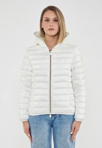 Giubbotto imbottito bianco con cappuccio e texture trapuntata. Presenta una chiusura frontale con zip e polsini a coste. Abbinato a jeans azzurri chiari.