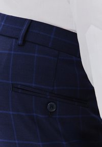 Granatowe spodnie w kratę, z zapinanym na guzik tylnym kieszeniami i gładką fakturą materiału. Dopasowany krój z prostymi nogawkami.