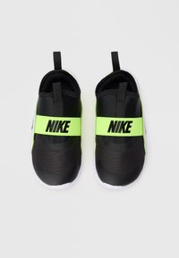 Chaussures Nike noires et vert fluo à enfiler avec une surface texturée, une sangle élastique et des semelles blanches ; design léger et minimaliste.