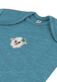 Hellblauer Baumwoll-Overall mit einem aufgestickten weißen Schaf-Patch und einem grünen vierblättrigen Kleeblatt-Akzent auf der Vorderseite.