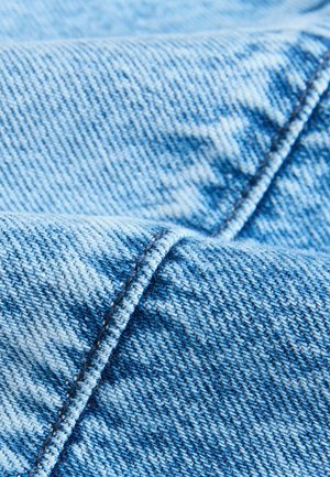 Helles blaues Denim-Gewebe mit einer strukturierten Webart und sichtbaren Nähten entlang der Kanten, das verschiedene Blautöne zeigt.