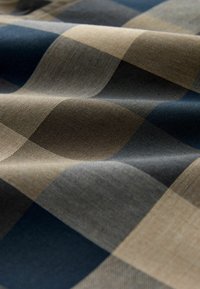 Geweefde stof met een ruitpatroon in beige, donker marineblauw en grijze tinten; zachte textuur met een lichte glans en een driedimensionaal uiterlijk.