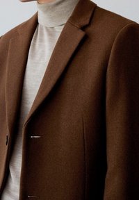 Brown wool blend blazer with notch lapels, single-breasted design, and two front pockets, layered over a light gray turtleneck sweater.