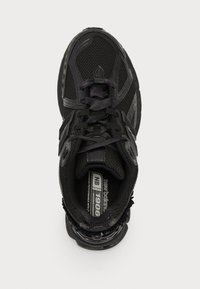 Chaussure de sport noire avec tige en mesh, col rembourré et bout renforcé. Présente des motifs texturés et des lacets avec une semelle rembourrée.