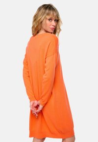 Robe-sweater en tricot orange avec des manches longues, coupe ample et ourlet arrondi. Texture douce et longueur mi-cuisse, conçue pour le confort.