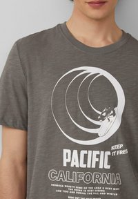 Grijze T-shirt met korte mouwen van zachte stof, met een witte surfontwerp met golven en de tekst "PACIFIC CALIFORNIA" eronder.