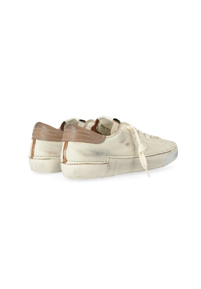Un paio di sneakers avorio con accenti di tacco in pelle marrone e lacci bianchi, che mostrano un aspetto leggermente usurato e vissuto.