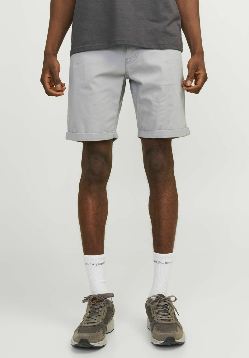 Pantalones cortos de algodón gris claro con puños enrollados, bolsillos frontales y diseño frontal plano, combinados con calcetines blancos y zapatillas grises.