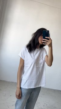 White short-sleeve t-shirt with a floral outline design in light thread. Straight cut, paired with light blue jeans, in a minimalistic setting.