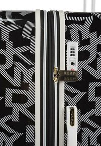 Maleta negra con patrón de rayas blancas y grises, con un cierre dorado y una cerradura de combinación. Acabado suave y brillante.