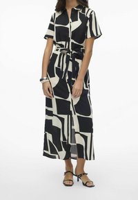 Vestido maxi de patrones en blanco y negro con mangas cortas, frente con botones y cintura ajustada. Tejido fluido con corte recto y detalle de abertura.