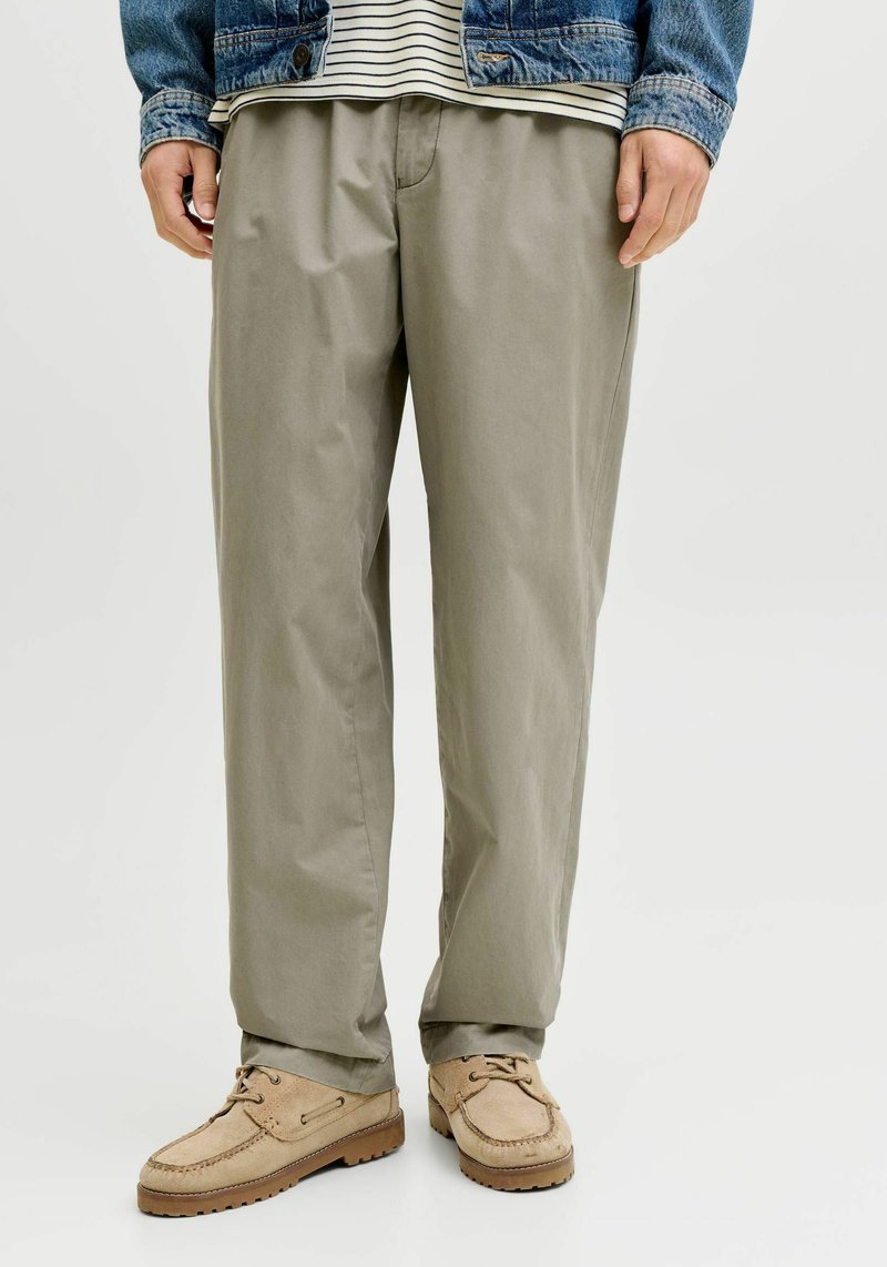 Pantalon en coton beige à coupe décontractée, avec une texture lisse et des poches latérales. Associé à des mocassins en daim beige clair.