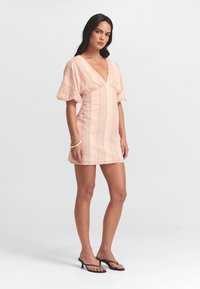 Vestido mini a rayas en rosa y blanco con un escote en V profundo, mangas cortas abullonadas y una silueta ajustada, combinado con chanclas negras.