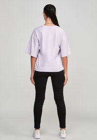 Ljuslila oversized kortärmad skjorta, kombinerad med svarta snäva jeans och vita sneakers, vilket visar en avslappnad passform och minimalistisk design.