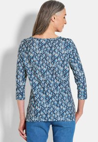Bluse mit blauem Muster und drei Viertelärmeln, die ein geometrisches Design in verschiedenen Blautönen zeigt, aus einem weichen, strukturierten Stoff gefertigt.