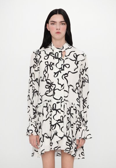 Witte jurk met zwart strikpatroon, lange mouwen, gerimpelde manchetten en een keyhole-halsdetail. Vloeiende silhouet met gelaagde zoomlijn.