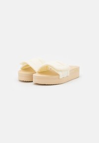 Light yellow platform sandals with padded, textured straps and a beige sole featuring a wavy tread pattern. Smooth, minimalist design.