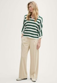 Haut rayé vert et blanc avec un col en V et des manches trois-quarts, associé à un pantalon beige à jambe large et des mocassins blancs.