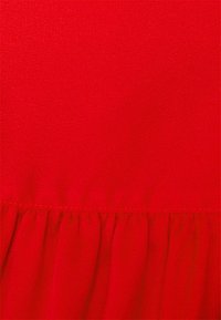 Červená látka s hladkým texturováním a mírným leskem. Obsahuje na spodní části nařasený lem, který vytváří rozšířený vzhled.