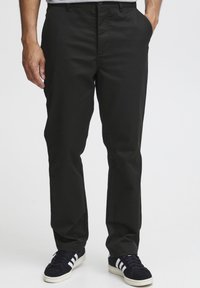 Black cotton-blend trousers with a straight-leg design, flat front, and side pockets, paired with black sneakers featuring white stripes.