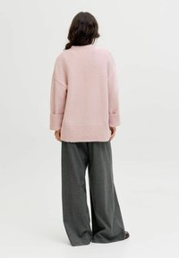 Suéter de punto rosa claro con un corte relajado, hombros caídos y puños acanalados. Llevado con pantalones grises de pierna ancha para un look en capas.