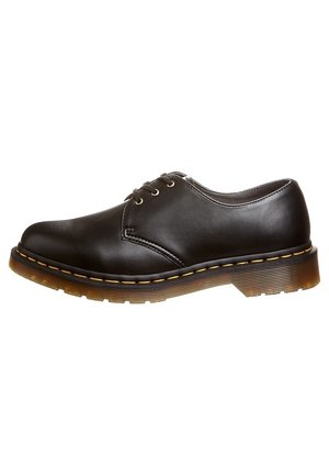 Chaussure Oxford basse en cuir noir avec trois œillets, couture jaune et semelle en caoutchouc marron translucide et épaisse.