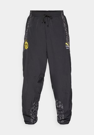 Čierne športové nohavice s viazaním v páse, s objímavým žltým logom a štruktúrovanými šedými detailmi na stranách. Ľahký materiál, zúžené nohavice.