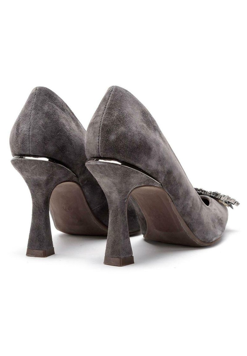 Un par de zapatos de tacón alto de ante gris con un acento metálico en la parte trasera y una hebilla decorativa en la parte delantera, mostrados desde la parte posterior.