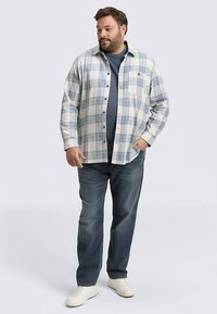 Camicia a quadri con bottoni in azzurro chiaro e bianco, abbinata a una t-shirt blu navy e jeans blu. Dotata di taschino singolo sul petto e bottoni neri.